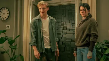 Brick (2025) movie: White German man left center stands next to Costa Rican German woman right, while in their living room