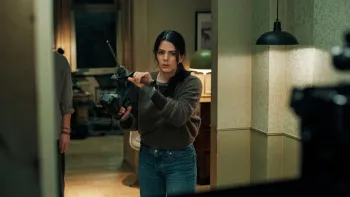 Brick (2025) movie: Costa Rican German woman stands in the hallway of her home holding a large drill