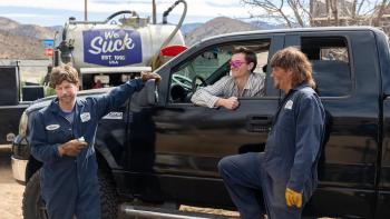 Busboys movie: Two men in dark work jumpsuits stand by a black truck in a desert area