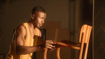 By Design Movie: Olivier (Mamoudou Athie) seems awestruck by the chair as he touches its wooden arms with his hands
