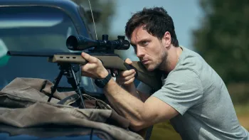 Fuze: A young man in a grey t-shirt aims a scoped rifle mounted on a bipod over the hood of a vehicle, outdoors in daylight