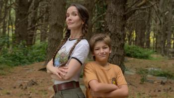 Camp Crasher movie: Spanish woman with long brown hair in two braids stands arms crossed back-to-back with smirking 12-year-old boy in white t-shirt