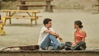 Camp Rock 3 Movie: Fletcher and Sage sit on a dock in a romantic mood, talking and smiling, with a guitar beside them.