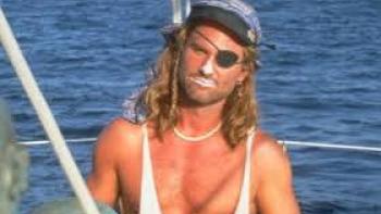 Captain Ron: Kurt Russell with an eye patch on a boat, wearing a bandana and necklace.