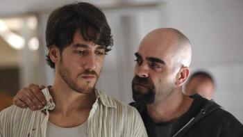 Cell 211 movie: Spanish bald man with goatee in black (right) has hand on shoulder of brown-haired Spanish man in light shirt (left)