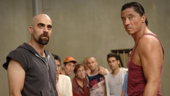 Cell 211 movie: With others behind them, Spanish bald man with goatee in black shirt left stands next to Spanish man in red shirt right