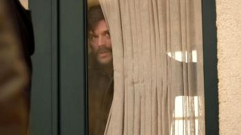 Chokehold: A Turkish man peaks out his window with light tan curtains
