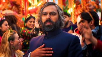 Christmas Karma: Man in dark formal attire at a festive gathering with colorful decorations and crowd in background