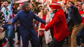 Christmas Karma: Two men dancing together at a festive Christmas party surrounded by celebrating crowd in holiday attire
