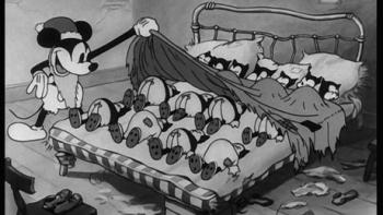 Still from Christmas with Walt Disney: Black-and-white scene from the 1932 Walt Disney short Mickey's Good Deed. Mickey Mouse is disguised as Santa Claus and looks at a bed filled with sleeping cat cartoon babies who are poor and later delivers holidays treats to them for Christmas