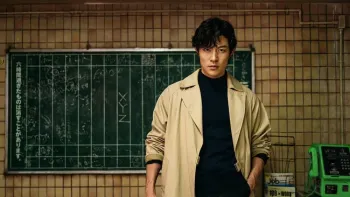 City Hunter movie: Japanese man in tan coat, black shirt stands in front of chalkboard with Japanese writing on it in columns
