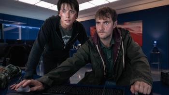 Cleaner: A battle-worn man and woman focus on a computer screen in a dimly lit room