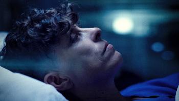 Come See Me in the Good Light movie: Andrea Gibson lies on a bed, their face profile to the audience