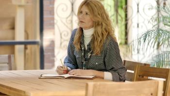 Common Ground Movie: Laura Dern sits at a table in a courtyard, contemplatively writing a letter
