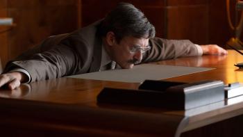 Corner Office Movie: Jon Hamm lies chest-down across a desk, resting on his chin, with his arms straight out to his sides on the desk