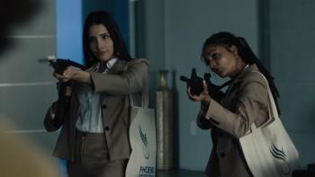 Corporate Retreat Movie: Wearing identical gray suits, Amber (Zión Moreno) and Lola (Sasha Lane) aim high-powered rifles