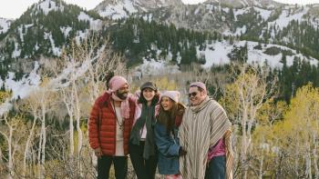 Couples Weekend movie: Daveed Diggs, Alexandra Daddario, Josh Gad, and Ashley Park stand together smiling in winter coats