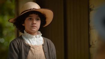 Cousins Movie: A young Māori woman gazes out from a porch, wearing a straw hat