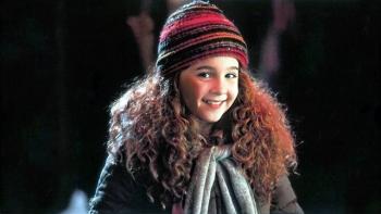 Curly Sue Movie: Curly Sue smiles, wearing a striped beanie and scarf in a dark, winter setting.