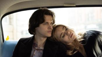 Daliland Movie: A young man in his 20s rides in the back of a car with a blonde woman, her head on his shoulder