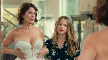 Daughter of the Bride Movie: A mirror reflects a woman trying on a low-cut bridal gown while a younger woman looks on.