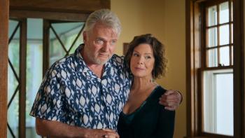 Daughter of the Bride Movie: A grey-haired man in a colorful print shirt holds has one arm around a woman's shoulder, holding her close while holding 