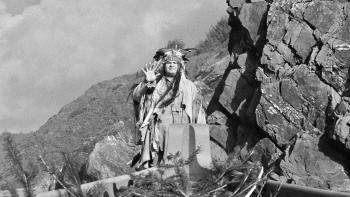 Dead Man: A Native American stands on a rock face with his hand held in the air