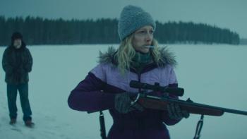 Dead of Winter movie: Judy Greer aims a rifle outside in the snow while sucking on a stick, a man standing behind her