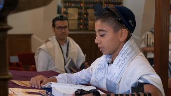 Dear Thirteen movie: Oren reads Torah, wearing white shirt, prayer shawl, blue yarmulke, and tefillin
