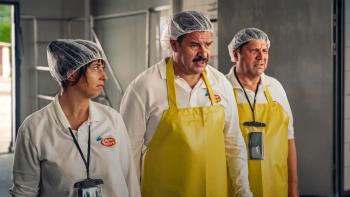 Death Before the Wedding: Mirek flanked by Karolina and Gajda, wearing dairy worker uniforms, clear hair covers, and bright yellow aprons,
