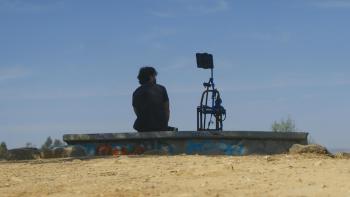 Deepfaking Sam Altman Movie: Seen from behind, Adam seems to be conversing with "Sambot," mounted on a kind of tripod