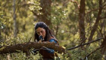 Die Alone Movie: Mae (Carrie-Anne Moss) crouches behind a branch and aims a rifle