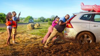 Disaster Holiday movie: South African Black man and woman push back of van right out of muddy ditch on side of road as their two children left look on