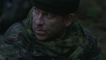 Dog Soldiers: Sean Pertwee sits in the forest dressed in green camouflage and a black hat looking sideways