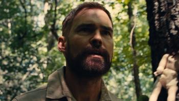Dolly Movie: In the woods, Chase (Seann William Scott) looks concerned; in the background, a doll is attached to a tree