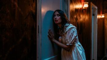 Dolly Movie: Wearing a doll-like dress and with blood on her face, Macy (Fabianne Therese) listens at a closed door