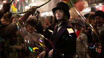 Dracula: Caleb Landry Jones is dressed formally as he looks around at the center of celebratory crowd