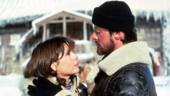 Rocky IV movie: Bearded Rocky in a shearling coat and beanie holds Adrian by the shoulders sweetly; snowy background