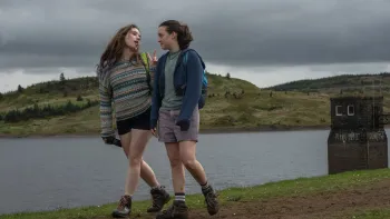 Sunny Dancer: Two teen girls walking by a lake on a cloudy day, wearing casual outdoor clothing