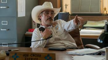 Eddington Movie: Sheriff Joe Cross (Joaquin Phoenix) sits at his desk, holding a phone receiver and pointing at something