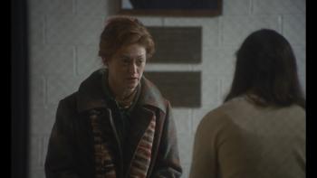 Eileen Movie: A middle-aged White woman speaks to a young woman in a grey, bleak building