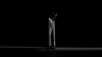 El Conde movie: In front of all pitch black background stands a Chilean military general in military garb, cape, and hat center looks downward