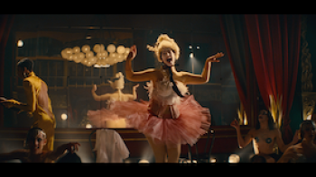 Still from Eldorado: Everything the Nazis Hate: A queer performer entertaining patrons on stage at Berlin, Germany's Eldorado nightclub, a hub for gays, lesbians, and trans individuals during the 1920s, wearing a pink pastel tutu, and a light-colored headdress and top
