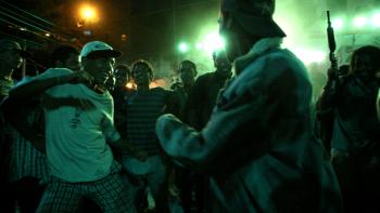 Elite Squad: A street party takes place under dark green lights while someone points a gun toward the night sky in the background