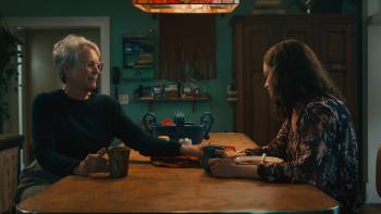 Ella McCay movie: Aunt Helen (Jamie Lee Curtis) holds Ella McCay's (Emma Mackey) hand across a kitchen table, comforting her