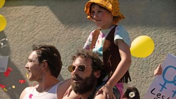Fairyland Movie: Young Alysia rides on her father's shoulders; balloons and signs are behind them, as if at a parade