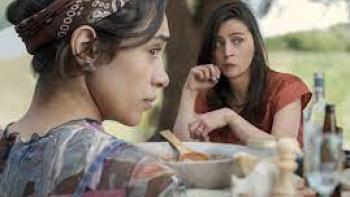 Familia scene 1: Two women sit across from each other at an outdoor table