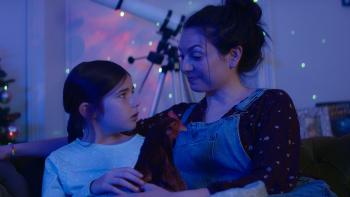 Feather Christmas: A dark room it lit with some small lights and a mother and daughter look at each other in conversation.