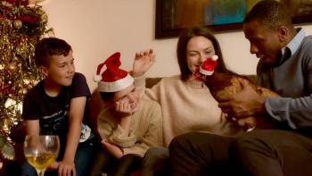 Feather Christmas : A group of people sit on a couch laughing with a Christmas tree behind them. A man holds a chicken.