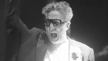 Fito Páez in a suit and glasses passionately gesturing with his arm raised.